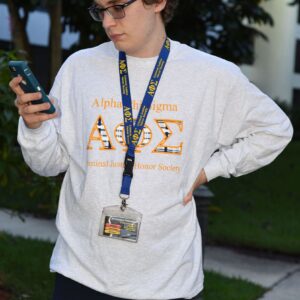 Person with phone wearing Alpha Phi Sigma shirt.